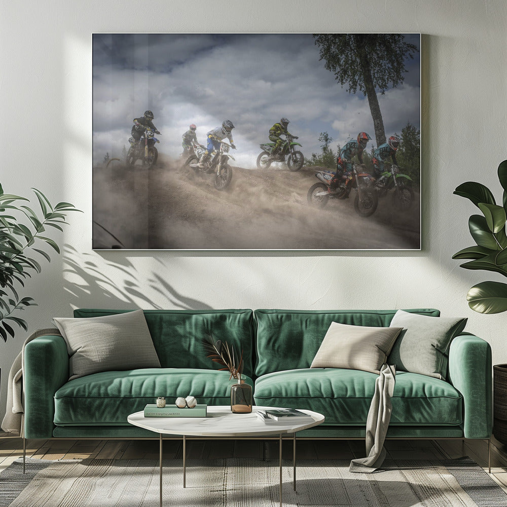 A dynamic action shot of several motocross riders racing up a dirt hill, kicking up a large cloud of dust. The riders are in full gear on colorful bikes, with a dramatic cloudy sky and a tall tree in the background. Print