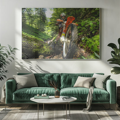A motocross rider on an orange dirt bike tackles a muddy, wooded trail, maneuvering around a moss-covered log in a lush green forest, seen from a low-angle perspective. Decor