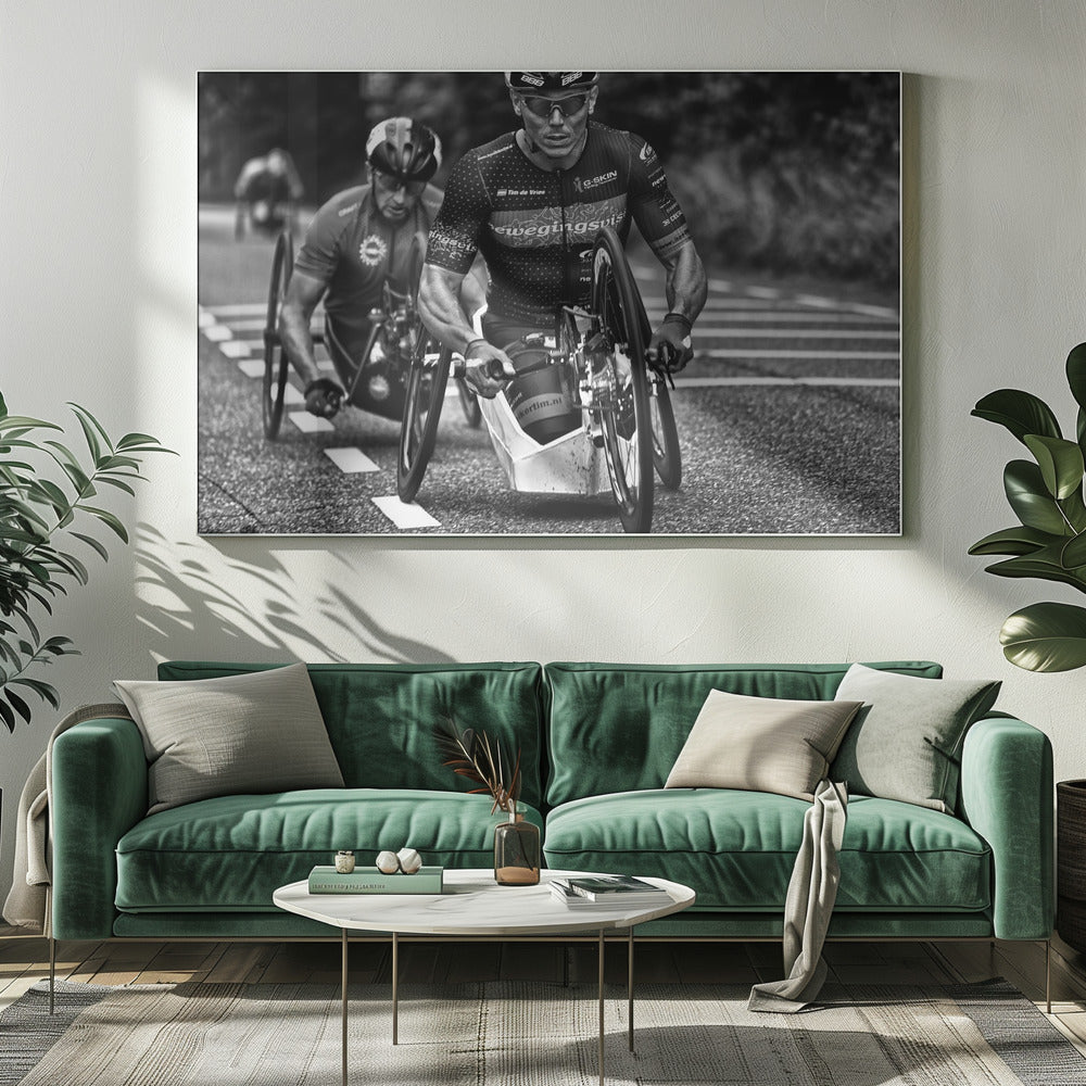 A powerful black and white photograph of two male athletes competing in a wheelchair race. The focused athlete in the foreground shows intense determination on his face, his muscular arms propelling the specialized racing wheelchair forward on an asphalt road. A second racer is visible in the background. Decor