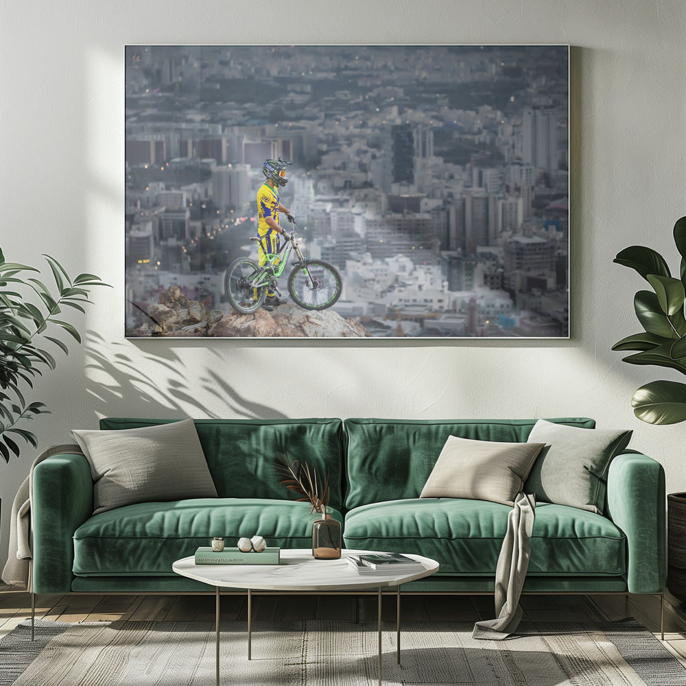 A mountain biker in a yellow and blue uniform stands with a green and white full-suspension bike on a rocky precipice, looking out over a vast, hazy cityscape that stretches into the distance. Print