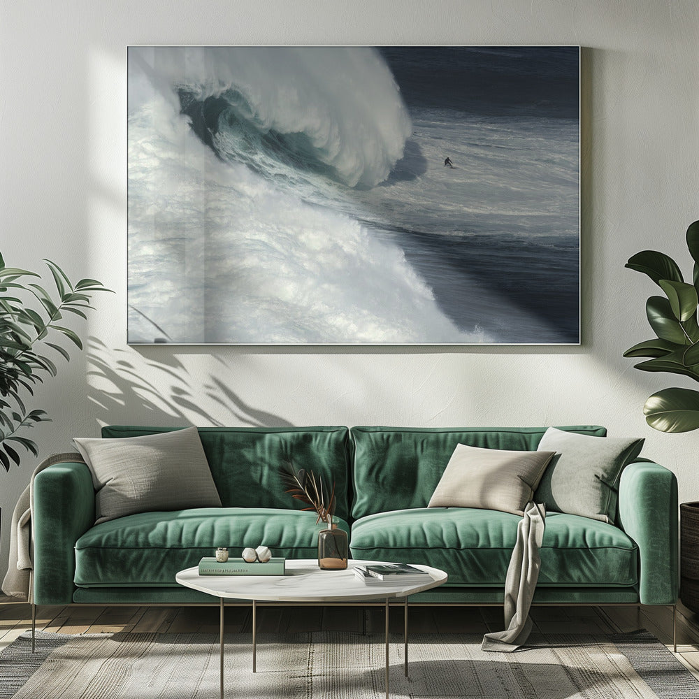 A framed aerial photograph captures a dramatic ocean scene where a lone surfer on a surfboard is dwarfed by an immense, powerful wave cresting nearby, conveying a sense of scale and adventure. Artwork