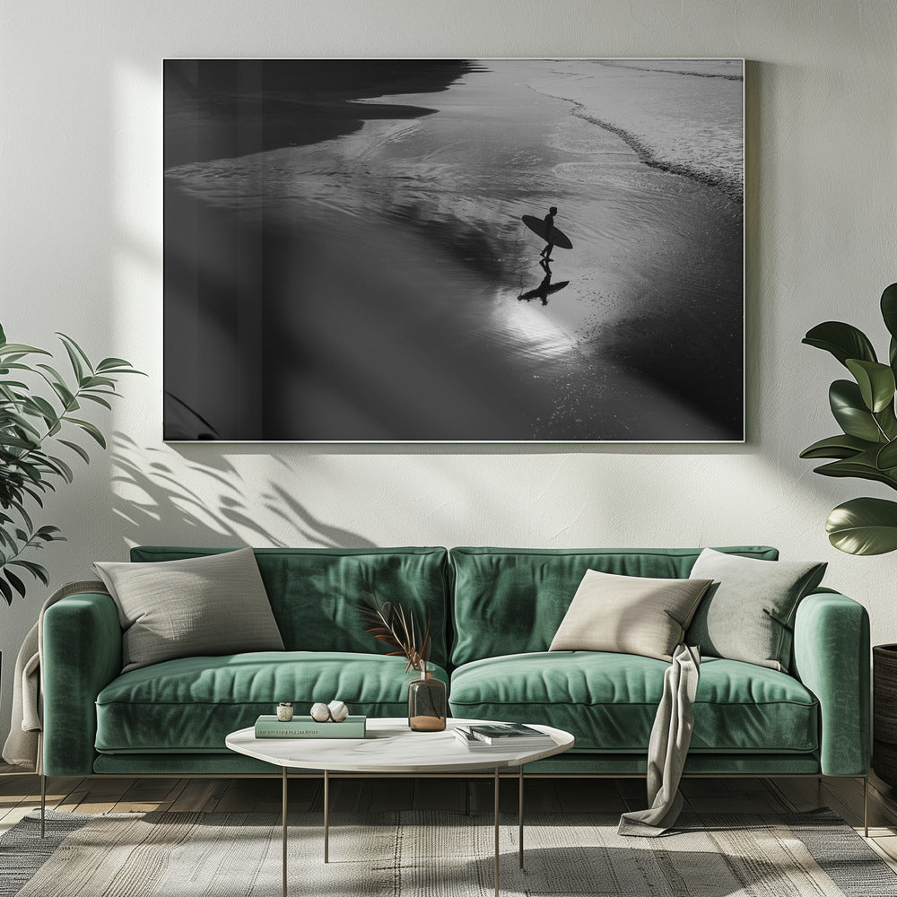 A high-contrast, black and white photograph of a silhouetted surfer carrying a surfboard and walking along the wet, reflective sand at the water's edge. Decor