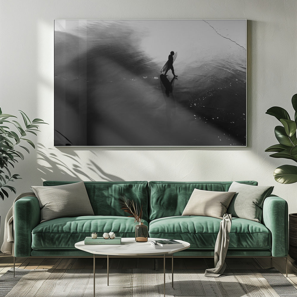 A high-contrast, black and white photograph of a surfer silhouetted against the bright reflection of the sun on the water. The surfer is carrying a surfboard and walking along the wet sand, leaving footprints behind. Their long shadow is cast in front of them on the dark, glistening sand. Print
