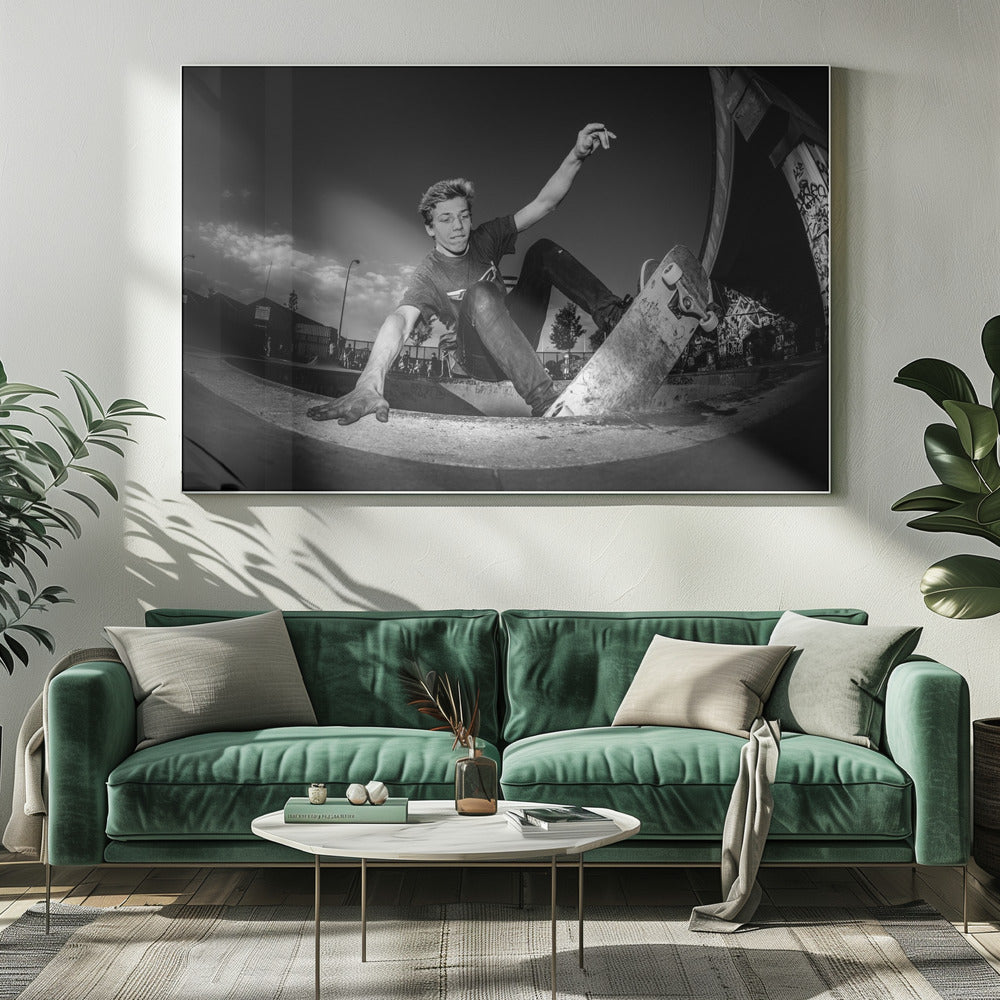 A dynamic, low-angle black and white action shot of a young skateboarder performing a trick in a concrete skatepark. He balances with one hand on the edge of the bowl, his body low to the ground as he carves along the curve, with his other arm raised in the air. Wall Art