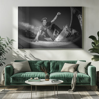 A dynamic, low-angle black and white action shot of a young skateboarder performing a trick in a concrete skatepark. He balances with one hand on the edge of the bowl, his body low to the ground as he carves along the curve, with his other arm raised in the air. Wall Art