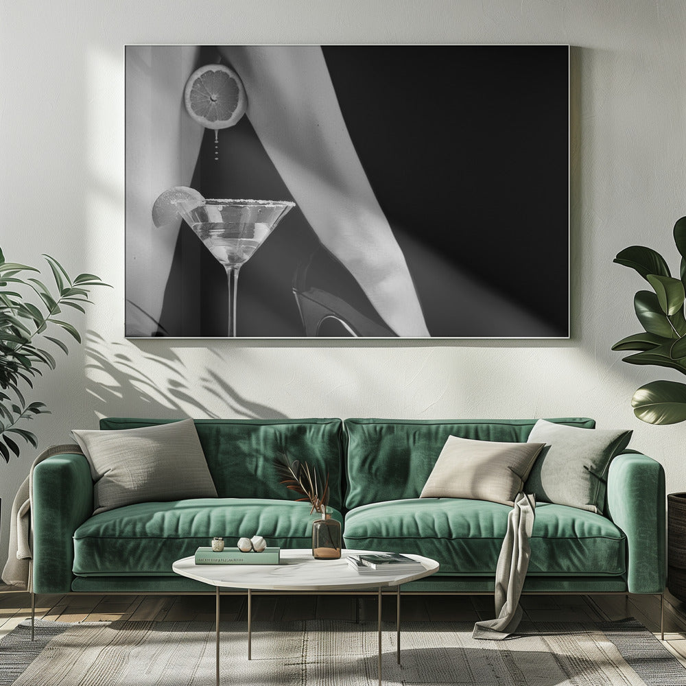 A framed, black and white photograph showing a woman's legs and a martini glass against a black background. A sliced citrus fruit is held between her thighs, with juice dripping towards the sugar-rimmed cocktail glass below. One foot is visible, wearing a black stiletto high heel. Artwork