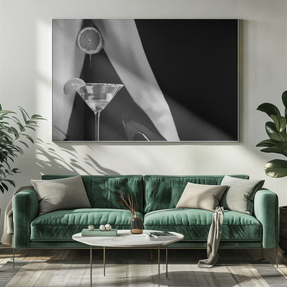 A framed, black and white photograph showing a woman's legs and a martini glass against a black background. A sliced citrus fruit is held between her thighs, with juice dripping towards the sugar-rimmed cocktail glass below. One foot is visible, wearing a black stiletto high heel. Artwork