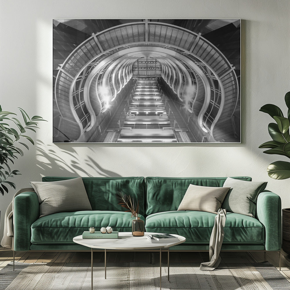 A symmetrical, low-angle black and white photograph of a futuristic escalator or grand staircase. The structure features illuminated, repeating curved arches on both sides, creating a tunnel-like perspective leading upwards. The image is presented within a silver-colored frame. Artwork