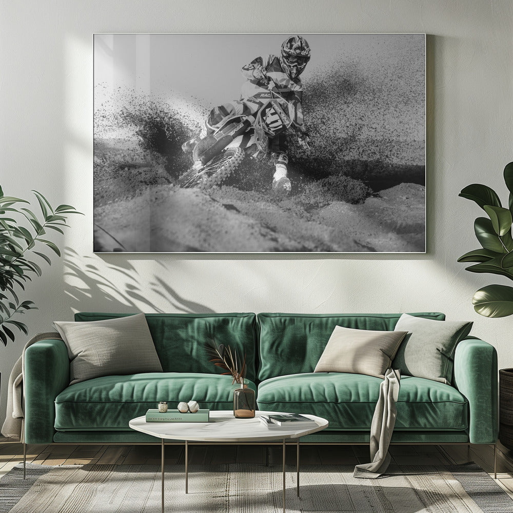 A dynamic black and white action photo of a motocross rider in full gear leaning hard into a turn, kicking up a large spray of dirt and sand from the track. The image is presented within a silver frame. Decor