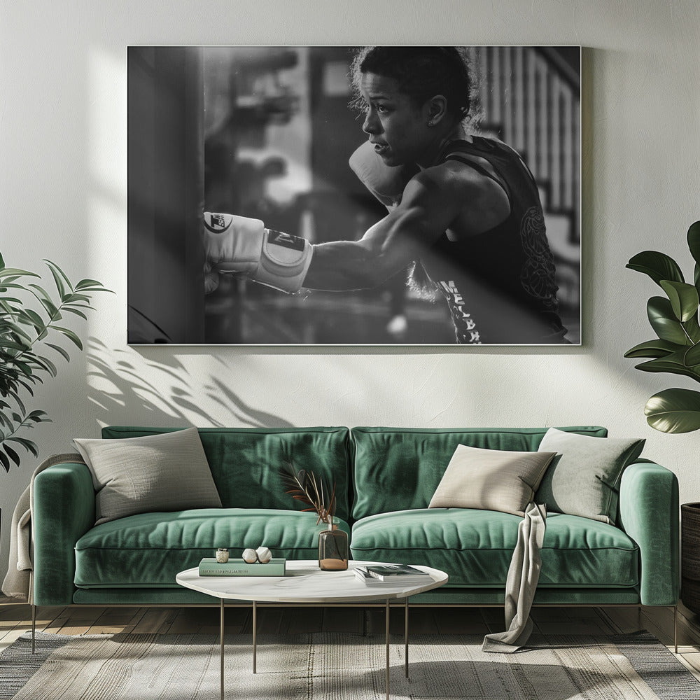 A dramatic black and white photo of a muscular female boxer in profile, intensely focused as she punches a heavy bag, set within a silver frame. Print