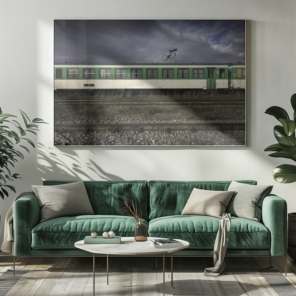 A BMX rider is captured in mid-air performing a stunt on the roof of a green and white passenger train car, set against a dramatic, stormy sky. The scene takes place on railway tracks with gravel and overgrown grass, and the entire image is enclosed in a silver frame. Decor
