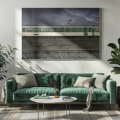 A BMX rider is captured in mid-air performing a stunt on the roof of a green and white passenger train car, set against a dramatic, stormy sky. The scene takes place on railway tracks with gravel and overgrown grass, and the entire image is enclosed in a silver frame. Decor