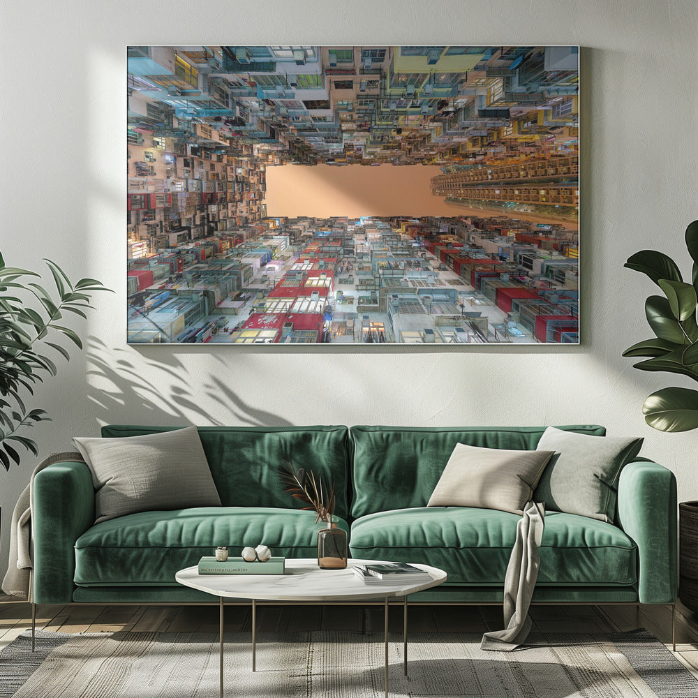 An upward-looking photograph from a courtyard surrounded by densely packed, multi-colored apartment buildings that create a rectangular frame around an orange sky. The unique perspective creates a surreal and geometric view of an urban landscape, all enclosed in a silver frame. Artwork