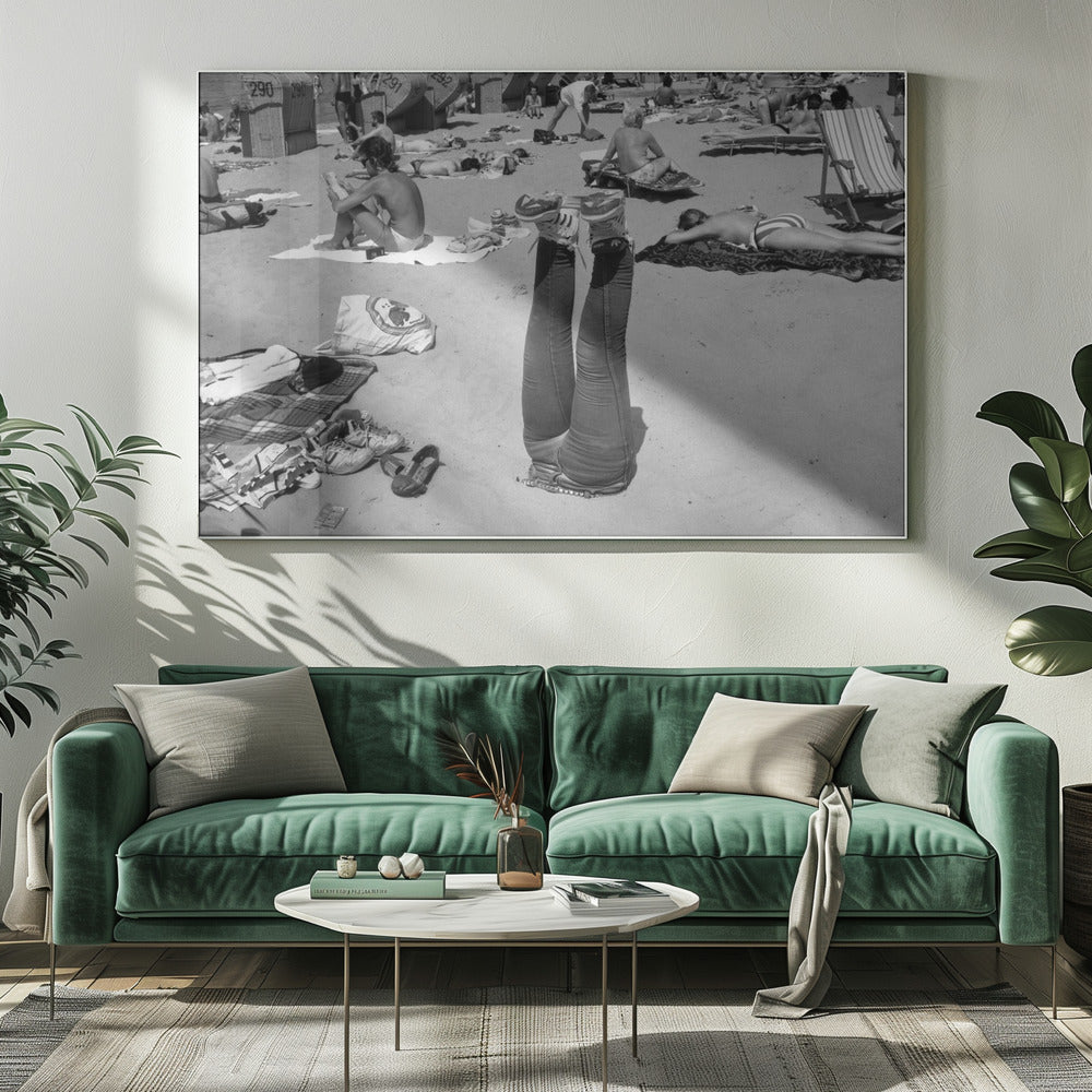 A quirky, vintage black and white photograph of a crowded beach. The central focus is a person lying on their back with their legs straight up in the air, oddly wearing jeans and sneakers. Surrounding them are numerous other beachgoers sunbathing on towels and in wicker beach chairs, creating a busy and candid summer scene. Wall Art