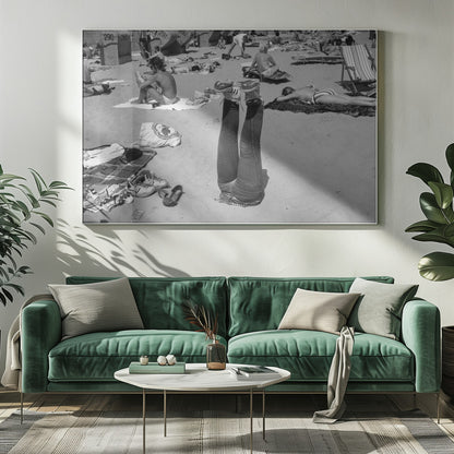 A quirky, vintage black and white photograph of a crowded beach. The central focus is a person lying on their back with their legs straight up in the air, oddly wearing jeans and sneakers. Surrounding them are numerous other beachgoers sunbathing on towels and in wicker beach chairs, creating a busy and candid summer scene. Wall Art