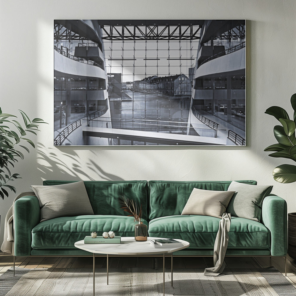 A symmetrical, black and white photograph taken from inside a modern building with curved balconies, looking out through a massive glass wall onto a canal and historic buildings on the opposite bank. A pedestrian bridge crosses the lower part of the frame. Decor
