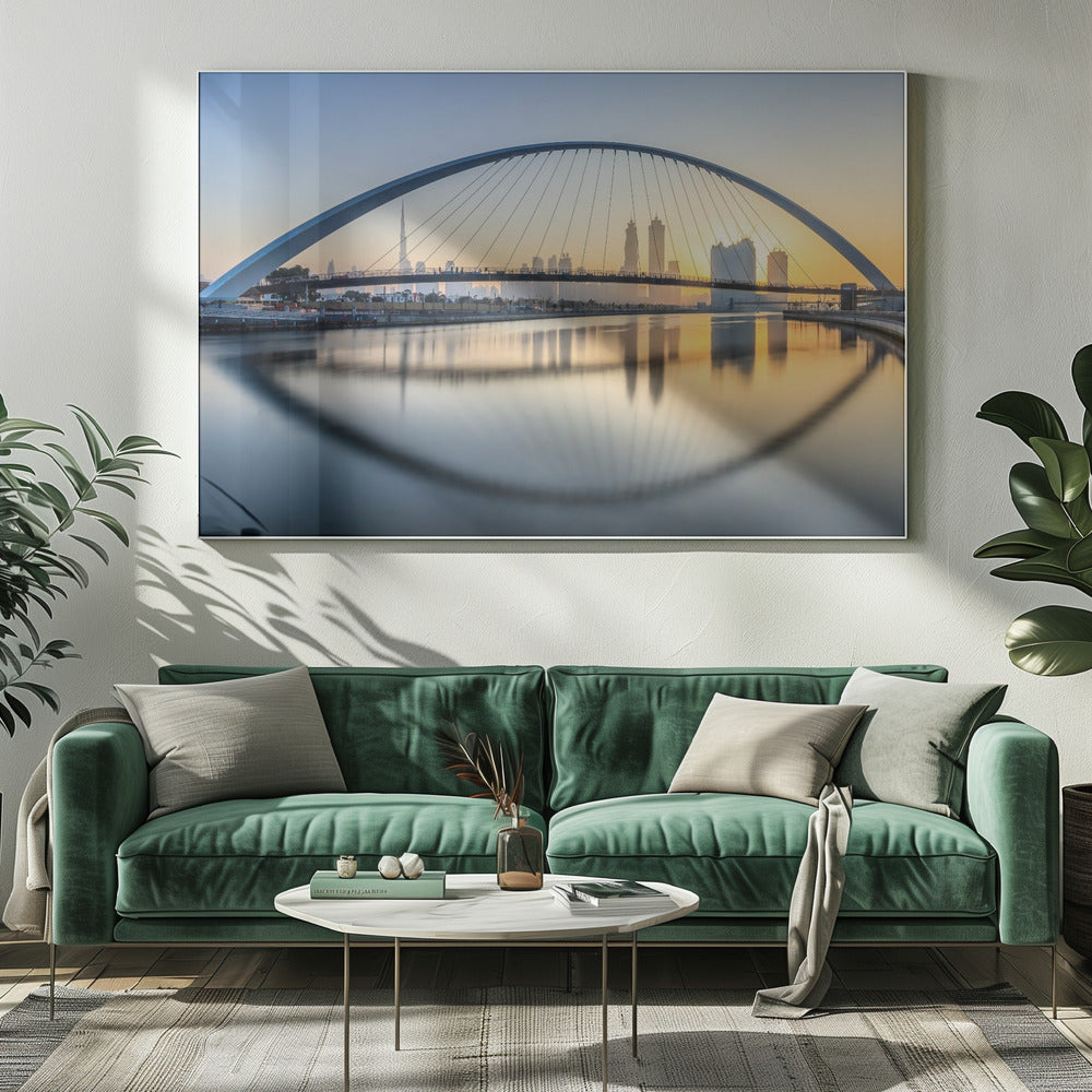 A framed photograph of the Dubai Water Canal Bridge at sunrise, with its large arch spanning across the water. The Dubai skyline, including the Burj Khalifa, is visible in the background, silhouetted against a golden and blue sky. The bridge and buildings create a perfect reflection on the calm surface of the water. Wall Art