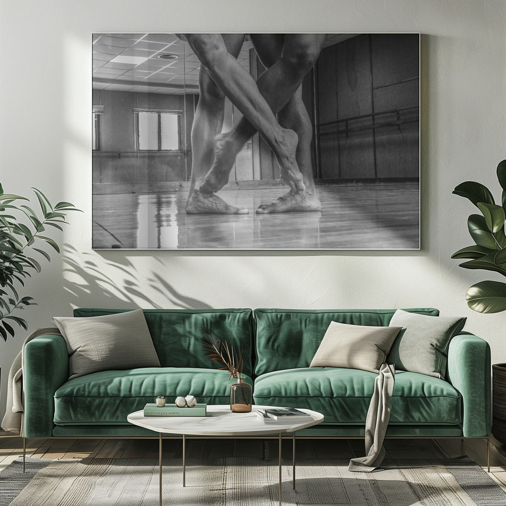 A dramatic low-angle, black and white photograph capturing the muscular legs and bare feet of two dancers intertwined in a dance studio. Their limbs cross in a display of strength and grace on a reflective wooden floor, with the studio's mirrored wall and barre visible in the background. The image is enclosed in a silver-grey frame. Decor
