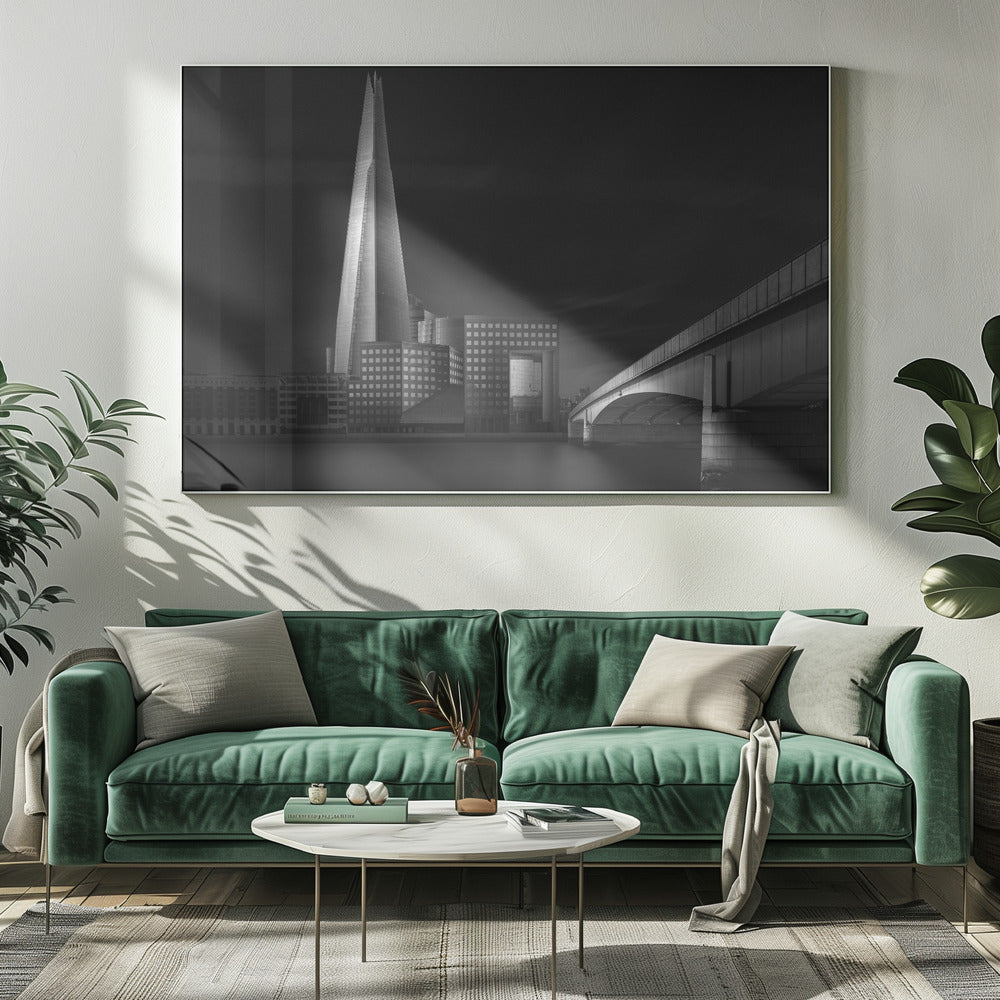A dramatic black and white photograph of the London skyline featuring The Shard skyscraper and London Bridge. The image is shot at dusk or night, with The Shard brightly lit against a dark, moody sky. The River Thames in the foreground is calm and reflective, captured with a long exposure. Artwork