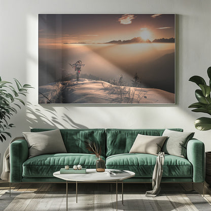 A lone person stands on a snowy mountain peak at sunrise, carrying a bicycle over their shoulder. They look out over a valley filled with a sea of clouds, with distant mountain ranges silhouetted against the bright, golden sun. Artwork