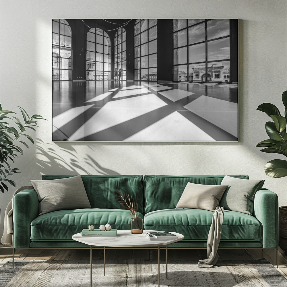 A striking black and white photograph of a spacious, modern hall with a polished floor. Dramatic shadows from large, arched windows are cast across the floor. Through the windows, a view of a classical European city with a triumphal arch can be seen. Print