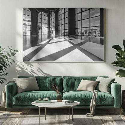 A striking black and white photograph of a spacious, modern hall with a polished floor. Dramatic shadows from large, arched windows are cast across the floor. Through the windows, a view of a classical European city with a triumphal arch can be seen. Print
