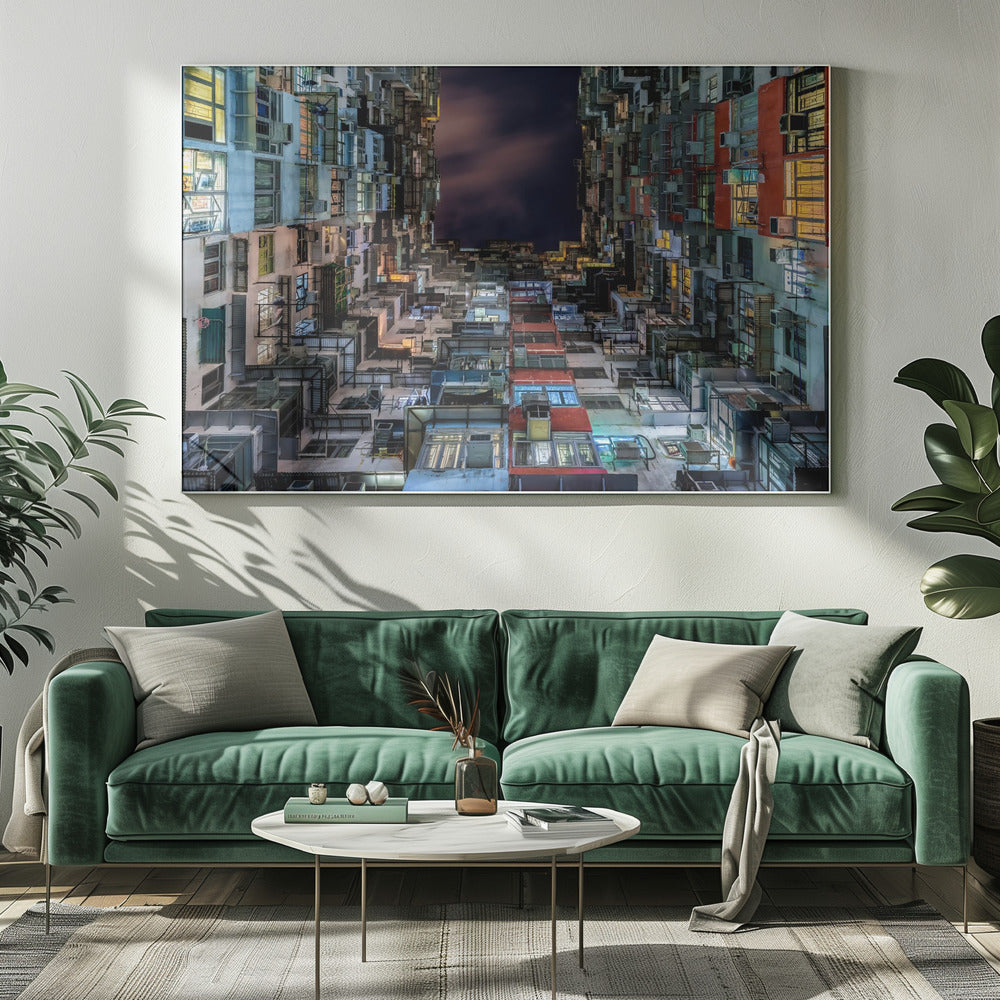 A low-angle nighttime view looking up from a courtyard surrounded by extremely dense, stacked apartment buildings with many windows lit in yellow, blue, and white, revealing a small patch of dark, cloudy sky. The image is presented within a brushed silver frame. Artwork