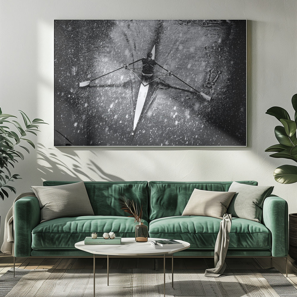 A dramatic black and white overhead photograph of a single rower in a narrow scull, captured mid-stroke as they cut through dark water during a heavy snowfall, creating a high-contrast and atmospheric scene. Decor