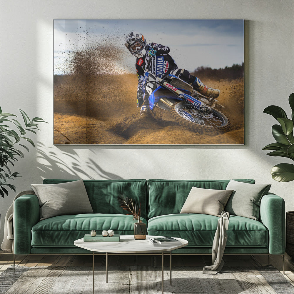 A motocross rider in full gear leans sharply into a turn on a dirt track, kicking up a large spray of mud and dirt from their blue and white Yamaha motorcycle. Artwork