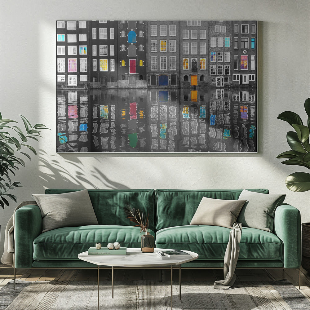 A framed black and white photograph of canal houses in Amsterdam, with selective coloring highlighting windows and doors in vibrant shades of red, blue, yellow, and pink. The colorful architectural details are mirrored in the rippling water of the canal below. Artwork