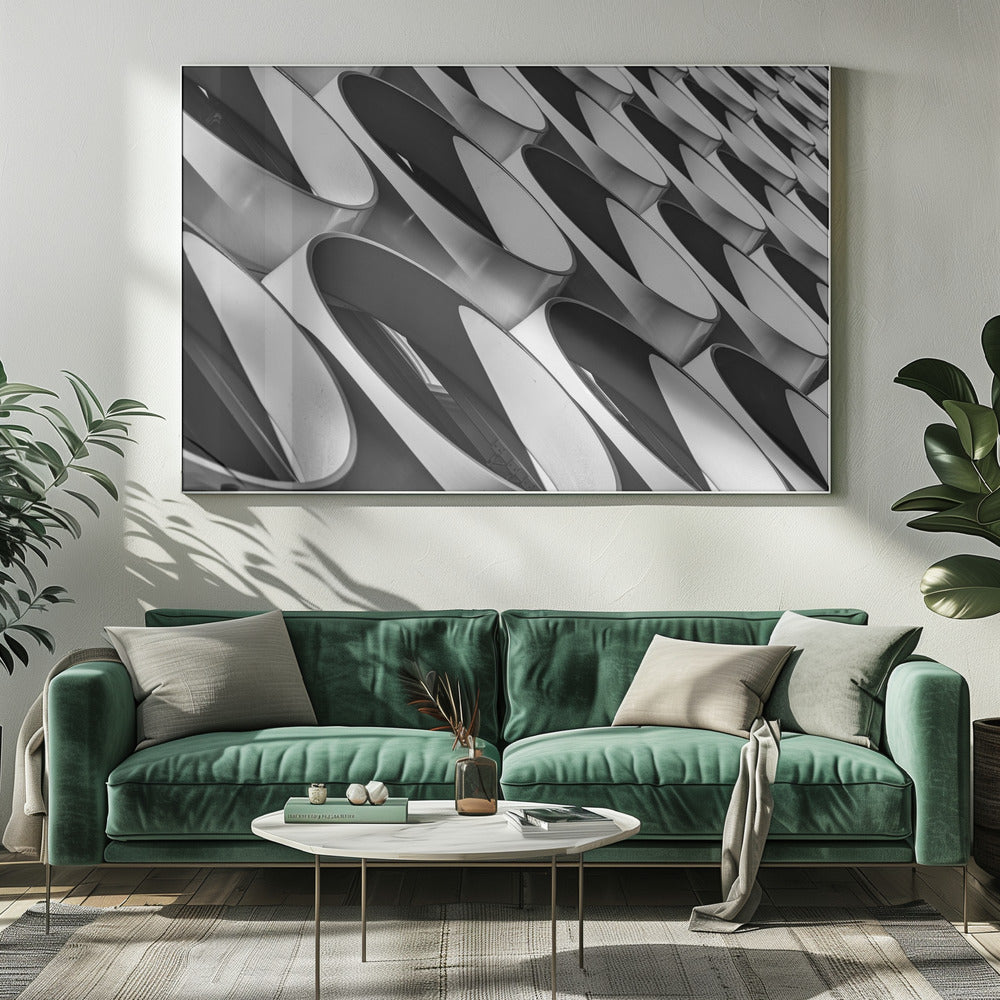 A framed, black and white photograph captures a low-angle, close-up view of a modern building's facade. The image features a repeating pattern of slanted, oval, or teardrop-shaped metallic elements, creating a dynamic interplay of light, shadow, and reflection. Print