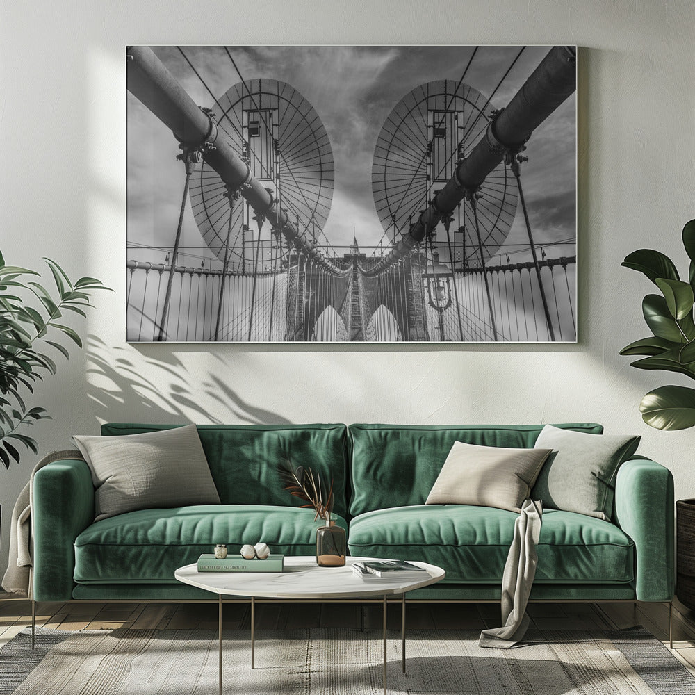 A symmetrical, low-angle black and white photograph of the Brooklyn Bridge's suspension cables and towers against a cloudy sky, framed in silver. Poster
