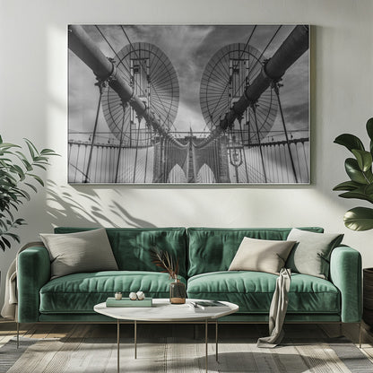 A symmetrical, low-angle black and white photograph of the Brooklyn Bridge's suspension cables and towers against a cloudy sky, framed in silver. Poster