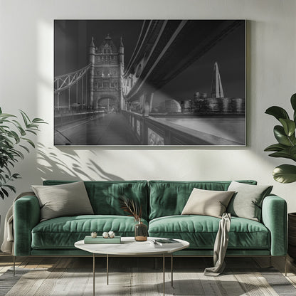 A dramatic, low-angle black and white photograph of London's Tower Bridge at night, taken from the pedestrian walkway. The image showcases the architectural details of the bridge and the illuminated modern city skyline, including The Shard, across the River Thames. Print