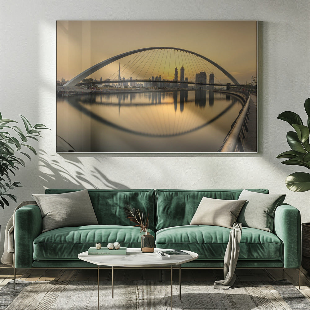 A sweeping view of the Dubai Water Canal Bridge at sunset, its white arch and cables stretching over the calm water. The city skyline, including the Burj Khalifa, is silhouetted against the golden sky, with the entire scene creating a perfect reflection in the water below. Print