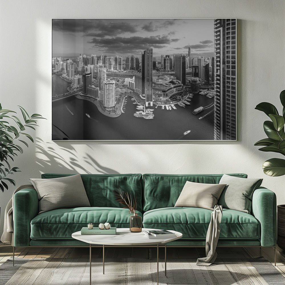 A framed, black and white panoramic photograph of the Dubai Marina taken from a high vantage point. The image captures the dense cityscape with numerous modern skyscrapers surrounding a winding waterway filled with docked yachts and moving boats. The sky is filled with dramatic, dark clouds, adding to the moody atmosphere of the urban landscape. Decor
