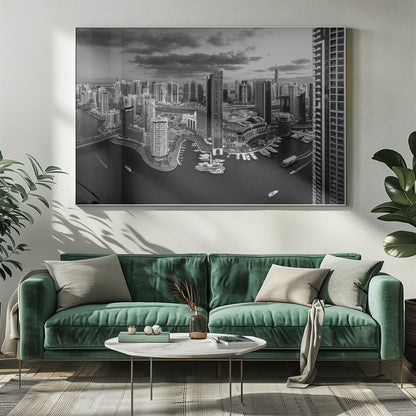 A framed, black and white panoramic photograph of the Dubai Marina taken from a high vantage point. The image captures the dense cityscape with numerous modern skyscrapers surrounding a winding waterway filled with docked yachts and moving boats. The sky is filled with dramatic, dark clouds, adding to the moody atmosphere of the urban landscape. Decor