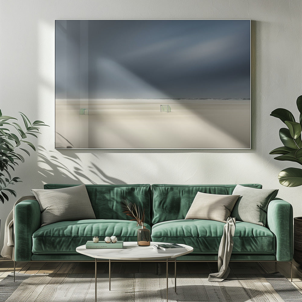 A minimalist long-exposure photograph of a vast, empty beach under a dark, moody sky. Two small, solitary soccer goals sit on the pale sand, with the ocean visible as a thin line in the distance. The artwork is presented in a silver frame. Artwork