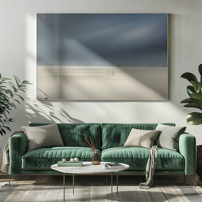 A minimalist long-exposure photograph of a vast, empty beach under a dark, moody sky. Two small, solitary soccer goals sit on the pale sand, with the ocean visible as a thin line in the distance. The artwork is presented in a silver frame. Artwork