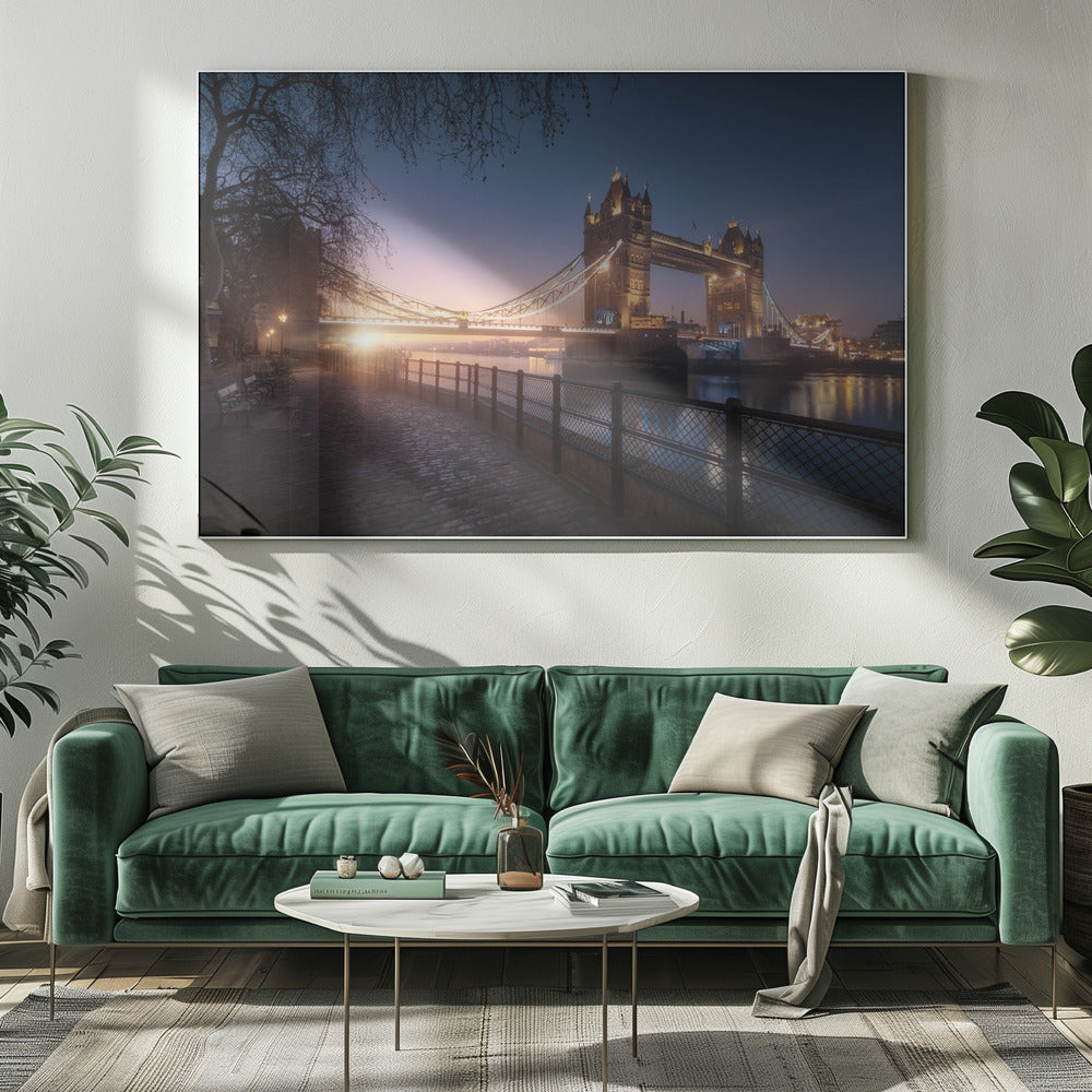 A scenic photograph of London's Tower Bridge at sunrise, its lights glowing warmly against a deep blue and orange sky. In the foreground, a cobblestone path follows the River Thames, leading the eye towards the iconic bridge and the rising sun. Poster