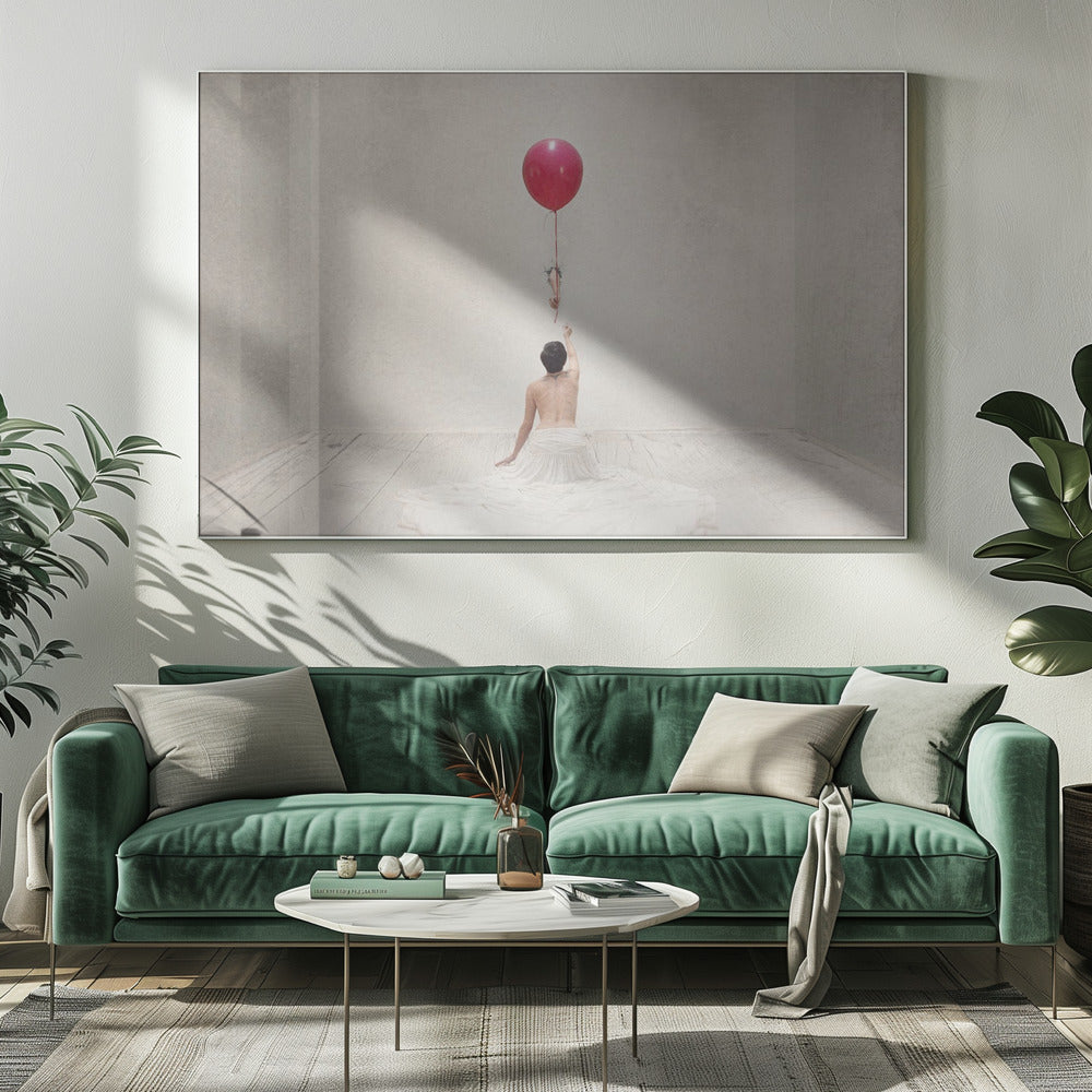 A surreal fine art photograph of a person with a bare back and a long white skirt, sitting on the floor of a minimalist grey room. They are reaching up towards a small figure hanging from the string of a large, bright red balloon that floats towards the ceiling. The image is enclosed in a silver frame. Artwork