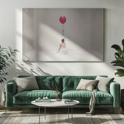 A surreal fine art photograph of a person with a bare back and a long white skirt, sitting on the floor of a minimalist grey room. They are reaching up towards a small figure hanging from the string of a large, bright red balloon that floats towards the ceiling. The image is enclosed in a silver frame. Artwork