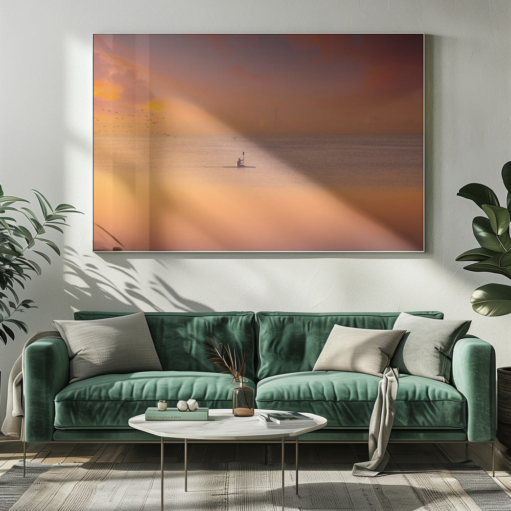 A serene photograph of a lone kayaker silhouetted against a vast expanse of calm water during a hazy, golden sunset. The sky and water are bathed in warm hues of orange, pink, and purple. A flock of birds flies in the distance, and the faint outline of a city skyline is visible on the horizon. Wall Art