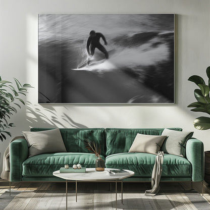 A dynamic black and white photograph of a surfer in a wetsuit carving through a wave. The image uses motion blur to emphasize the speed and energy of the water, creating a powerful and artistic effect. The artwork is presented in a simple silver frame. Print