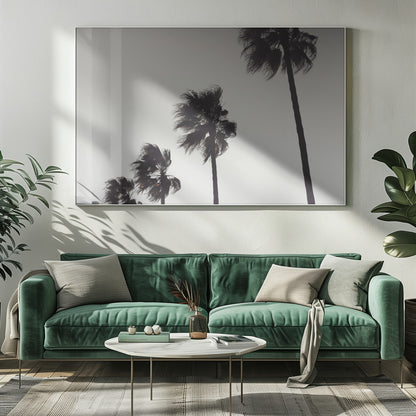A framed black and white photograph of four silhouetted palm trees of increasing height, arranged diagonally against a plain, light grey sky. The palm fronds are blurred, suggesting they are blowing in the wind. Decor