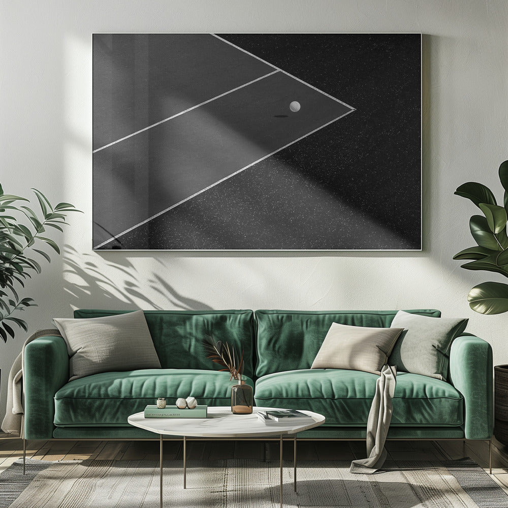 A minimalist black and white overhead photograph of a white ball resting in the corner of a dark tennis or paddle court. The composition focuses on the strong geometric angles created by the white boundary lines against the dark, textured asphalt, all within a silver frame. Artwork