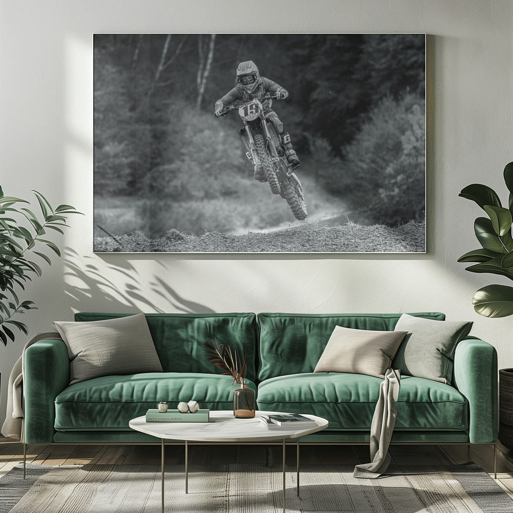 A dynamic black and white photograph of a motocross racer in mid-air, jumping over a dirt mound. The rider, wearing full protective gear and a helmet, is on a dirt bike with the number 19 plate. The background is a soft-focus forest, and the entire image is enclosed in a silver frame. Poster