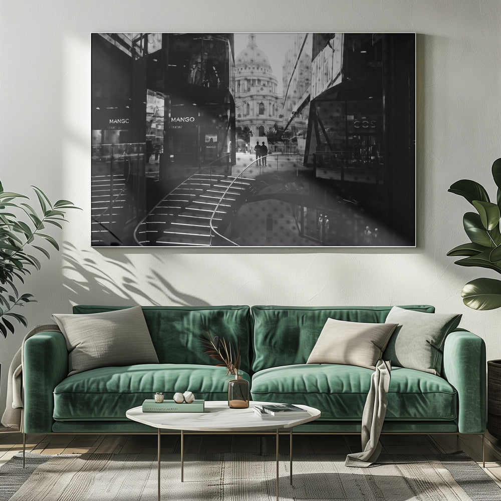 A framed, black and white photograph capturing a layered urban scene. The view, seen through a window with reflections of a curved, lit staircase, shows two people walking towards a large domed cathedral framed by modern glass buildings. Wall Art