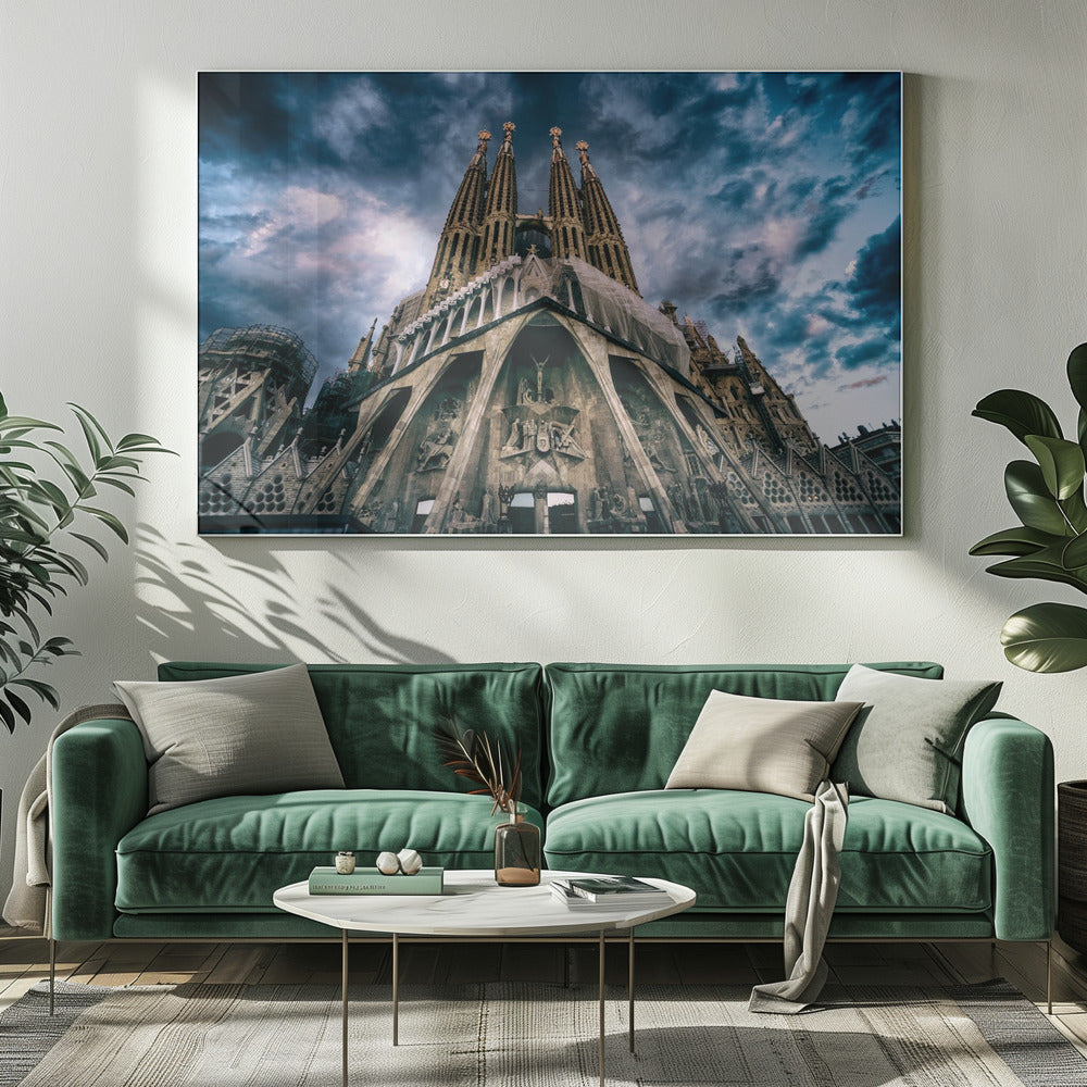 A dramatic, low-angle photograph of the Sagrada Familia in Barcelona, with its ornate stone facade and towering spires reaching up into a turbulent, dark blue and cloudy sky. The perspective emphasizes the grand scale and intricate detail of Gaudí's architecture. Print