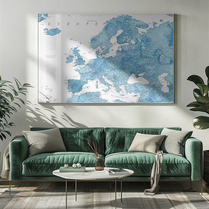 A framed map of Europe with a blue watercolor texture. The land is depicted in various shades of blue, while the oceans are white. Countries, cities, and bodies of water are labeled in black text. The map is housed in a simple, light gray frame. Poster